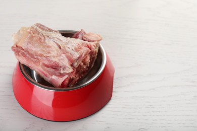 Photo of Feeding bowl with raw chopped meaty bones on white wooden table. Space for text