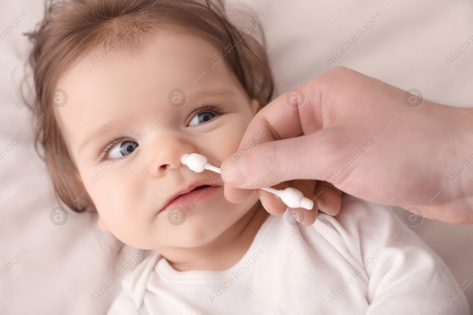 Photo of Father cleaning nose of his baby with cotton bud on bed, top view