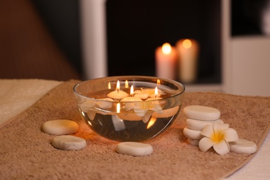 Bowl with water and burning candles on table in spa salon