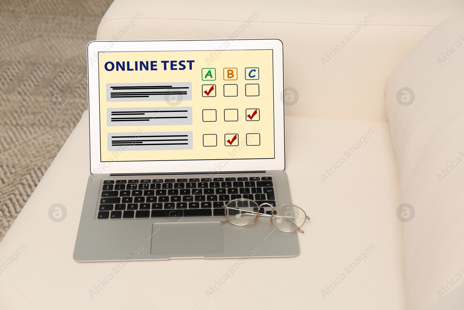 Photo of Laptop with online test and glasses on sofa in living room