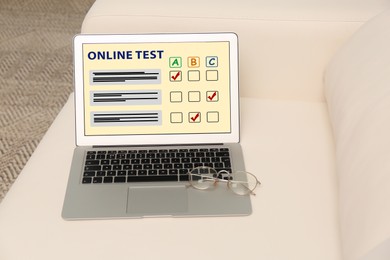 Laptop with online test and glasses on sofa in living room