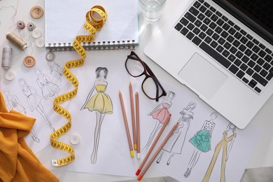 Sketches of clothes and different stuff on white table, flat lay. Fashion designer's workplace