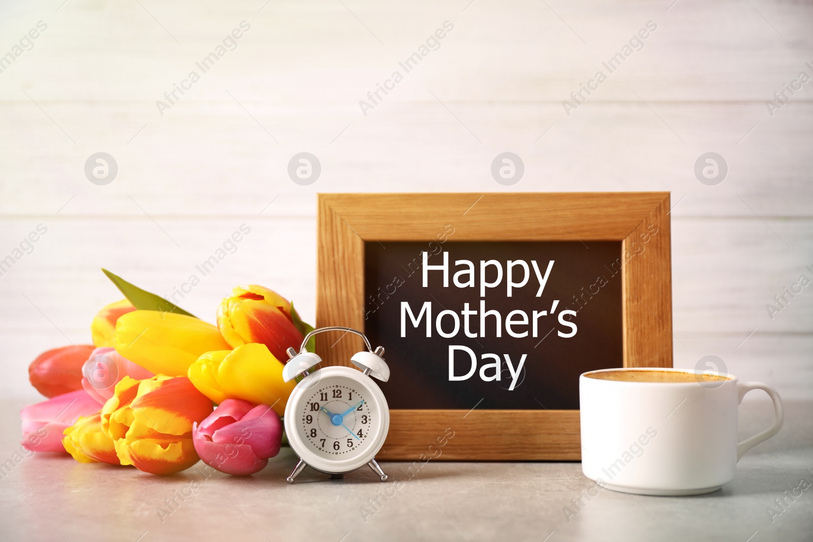 Image of Chalkboard with phrase HAPPY MOTHER'S DAY, tulips, cup of coffee and alarm clock on light table