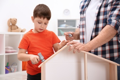 Photo of Man and his child playing builders with wooden doll house at home