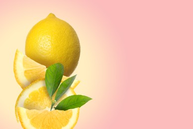 Cut and whole fresh lemons with green leaves on pink background, space for text