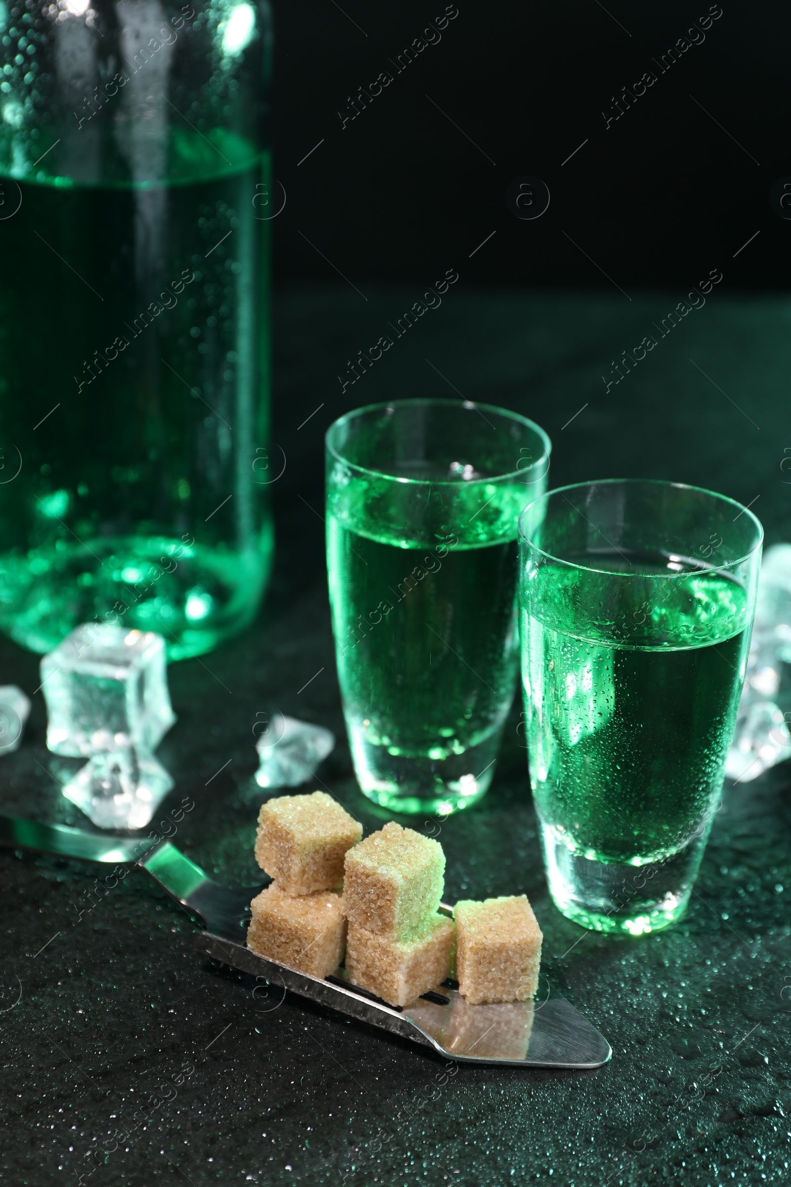 Photo of Absinthe in shot glasses, spoon, brown sugar and ice cubes on gray table. Alcoholic drink