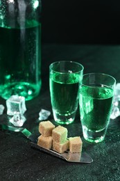 Photo of Absinthe in shot glasses, spoon, brown sugar and ice cubes on gray table. Alcoholic drink