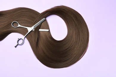 Lock of brown straight hair and thinning scissors on color background, flat lay