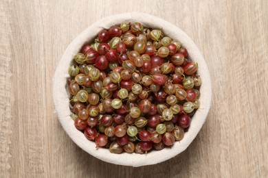 Photo of Fresh ripe gooseberries in bowl on wooden table, top view