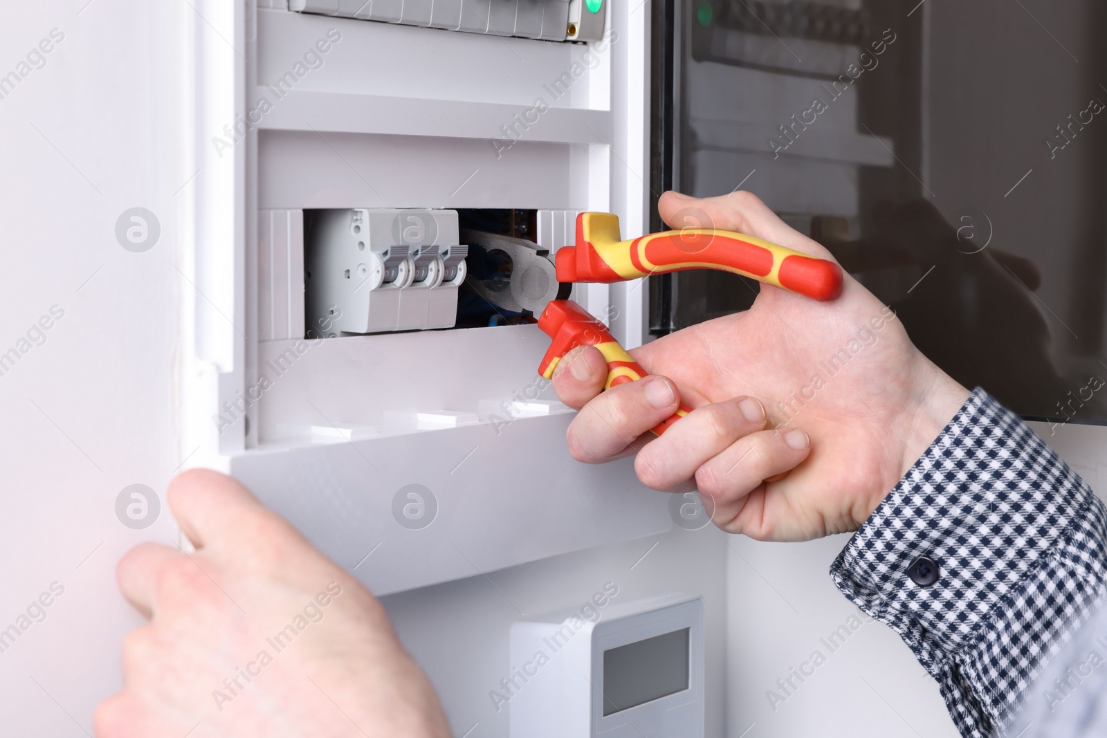 Photo of Professional repairman fixing electric panel with pliers indoors, closeup