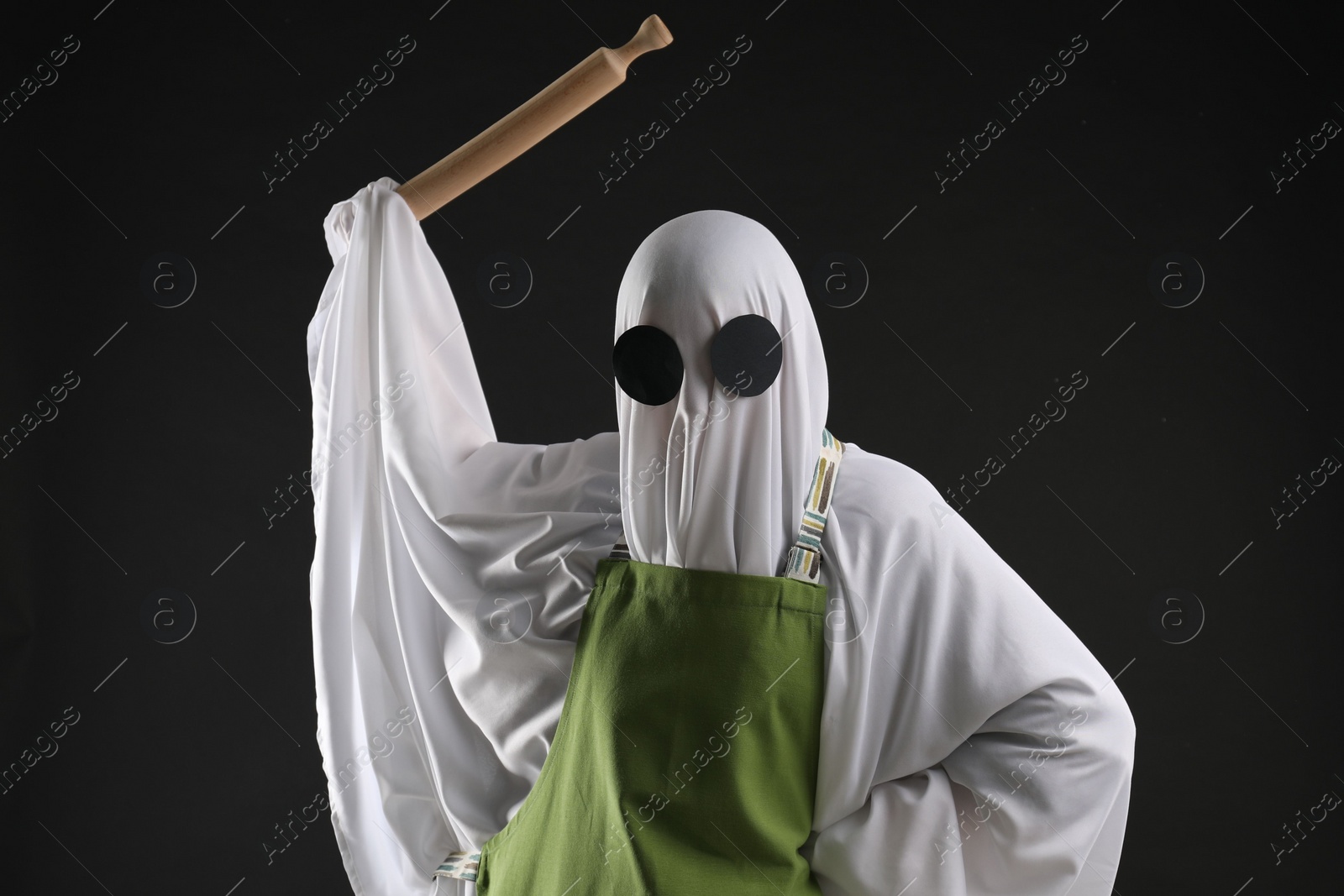 Photo of Woman in ghost costume and apron with rolling pin on black background