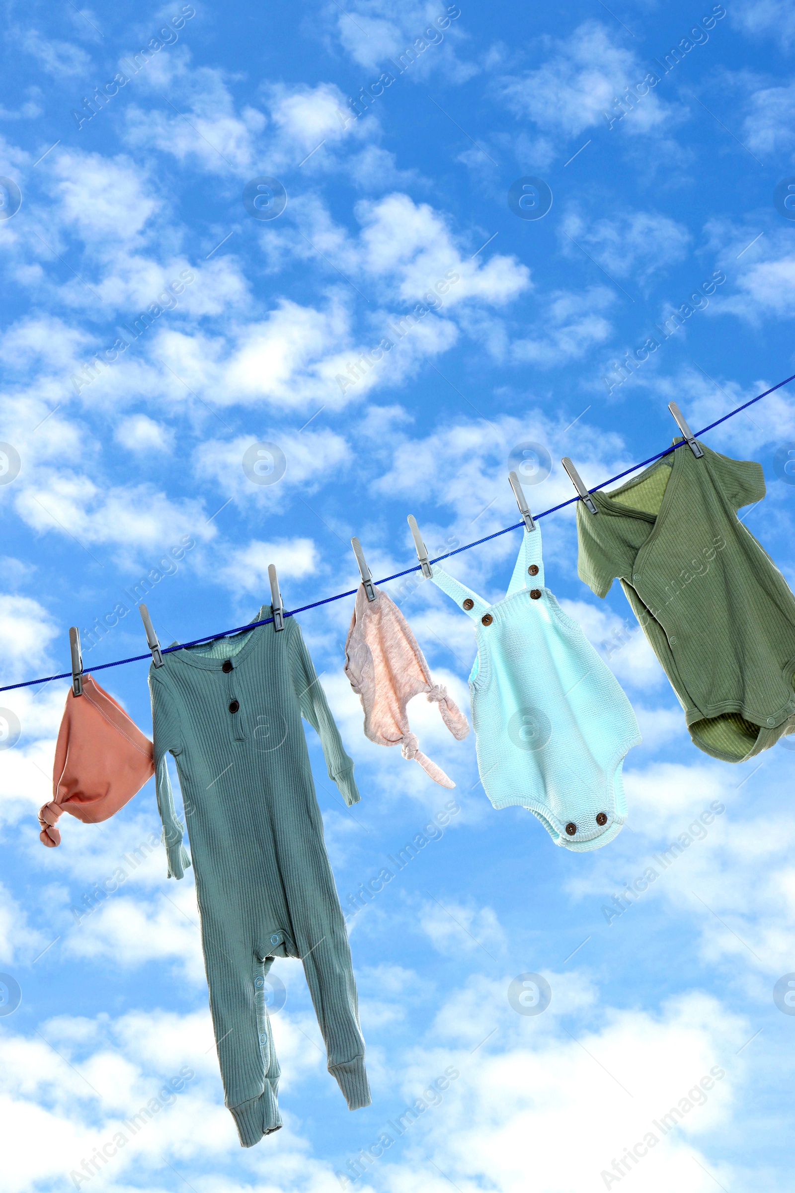 Image of Different baby clothes drying on washing line against sky