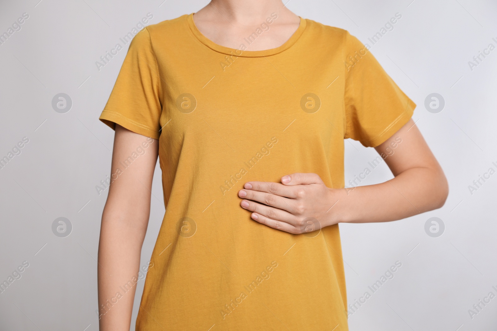 Photo of Woman holding hand near stomach against grey background, closeup