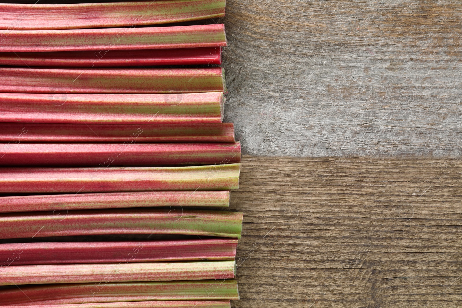 Photo of Fresh rhubarb stalks on wooden table, top view. Space for text
