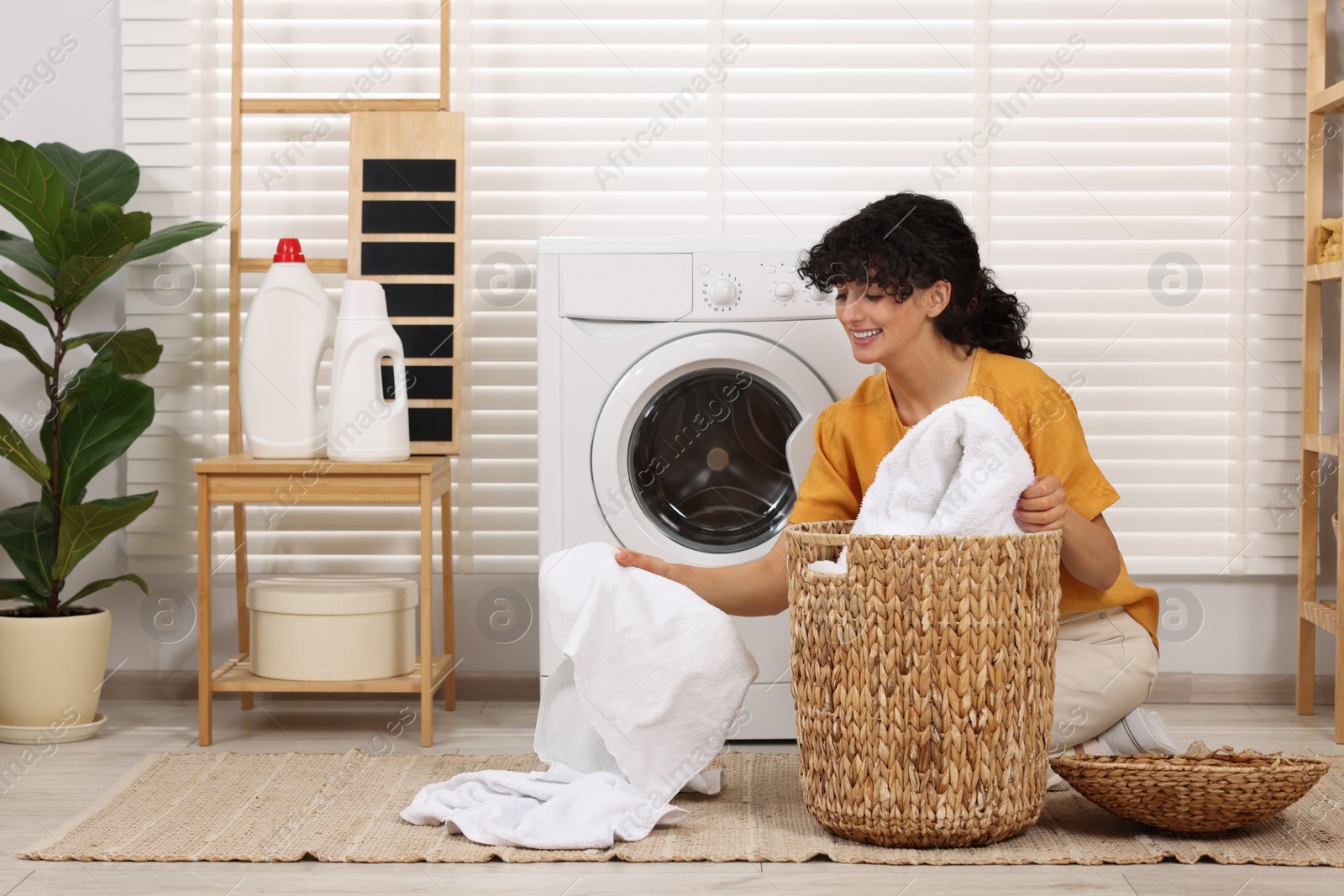 Photo of Happy woman with laundry near washing machine indoors