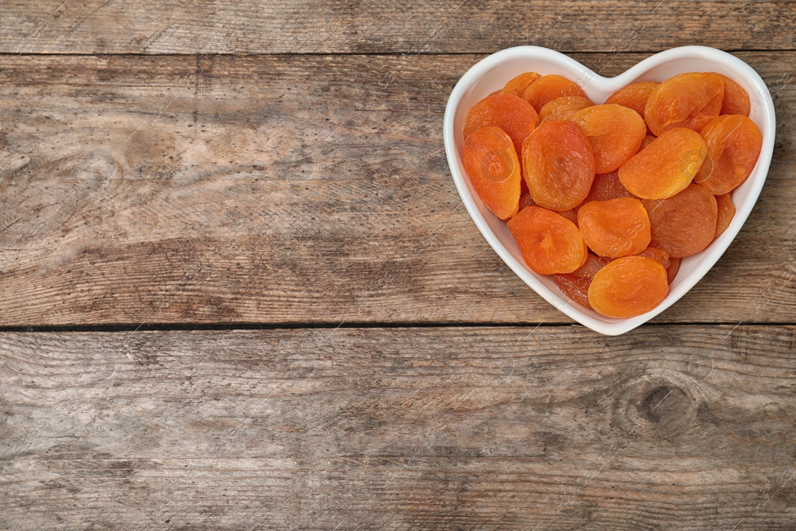 Photo of Bowl of dried apricots on wooden table, top view with space for text. Healthy fruit