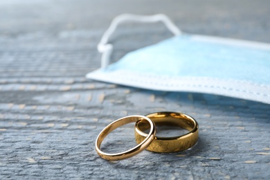 Photo of Wedding rings and protective mask on grey wooden table, space for text. Divorce during coronavirus quarantine