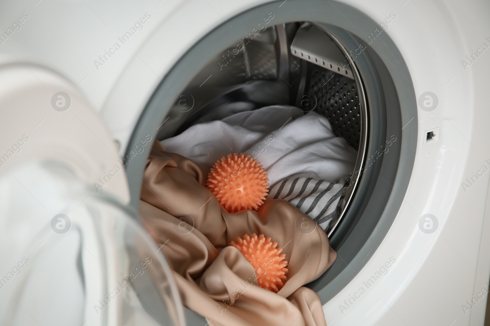 Photo of Dryer balls and clothes in washing machine, closeup