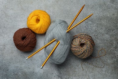 Soft woolen yarns and knitting needles on grey table, flat lay