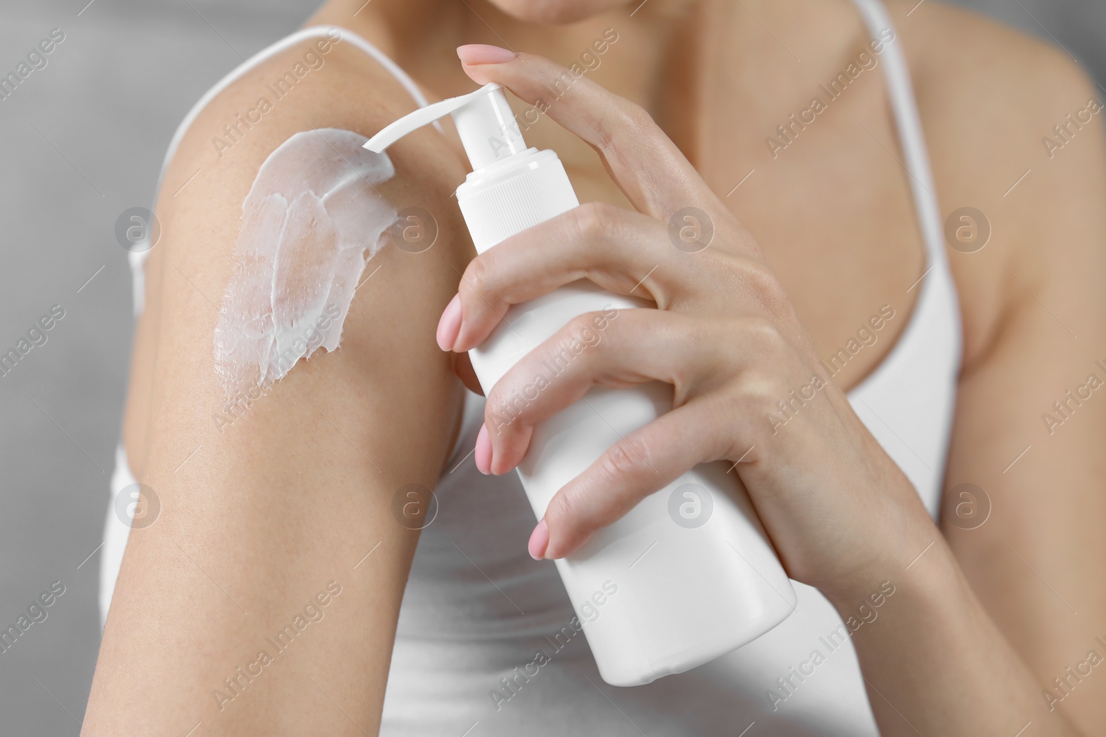 Photo of Woman applying body cream onto shoulder on grey background, closeup