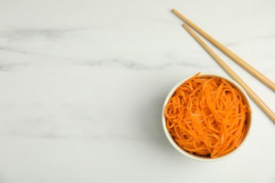 Photo of Delicious Korean carrot salad and chopsticks on white marble table, flat lay. Space for text