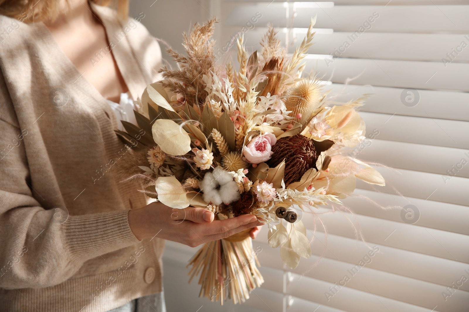 Photo of Woman holding beautiful dried flower bouquet near window at home, closeup