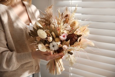 Woman holding beautiful dried flower bouquet near window at home, closeup