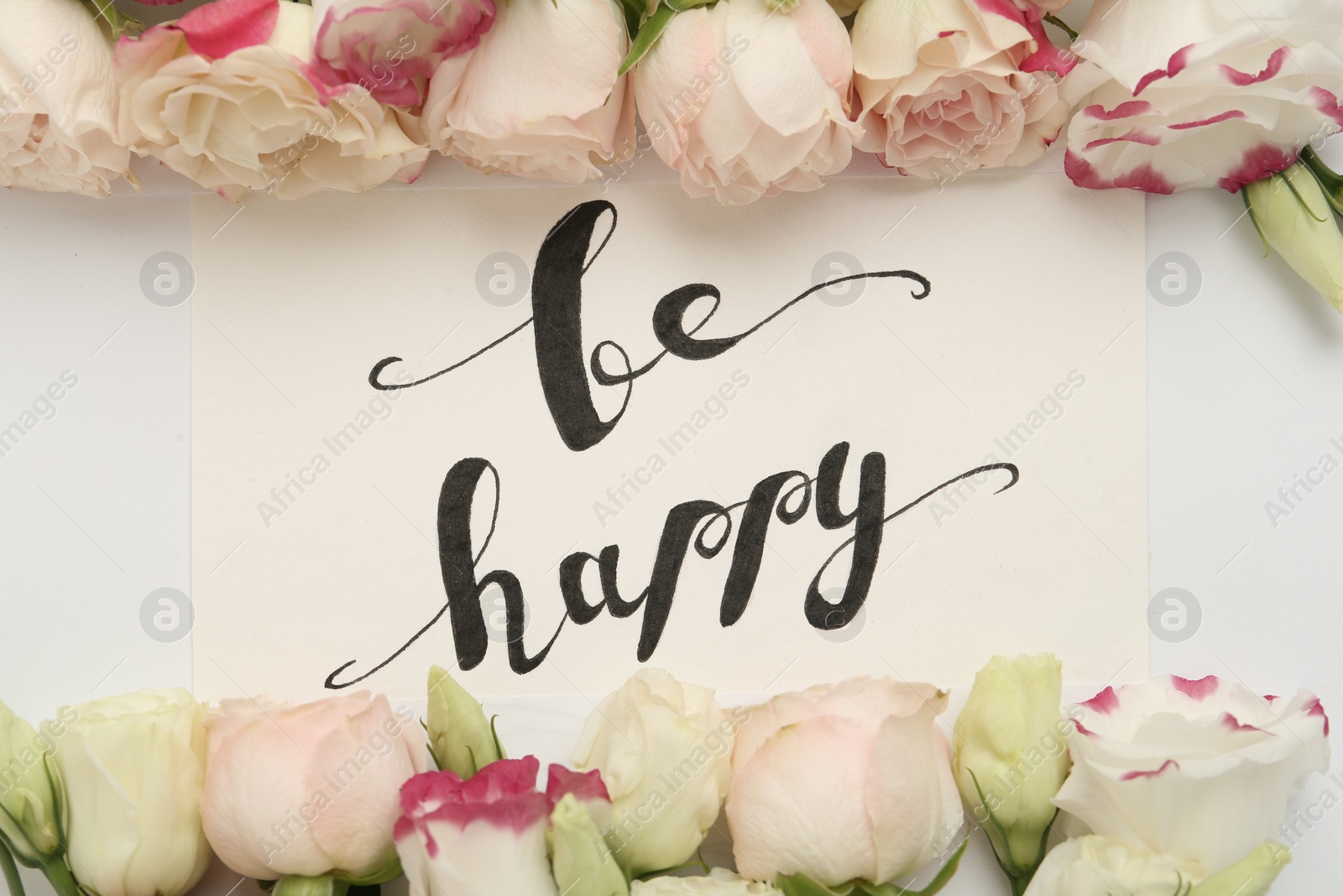 Photo of Frame of beautiful flowers and paper card with handwritten text Be happy on white background, flat lay