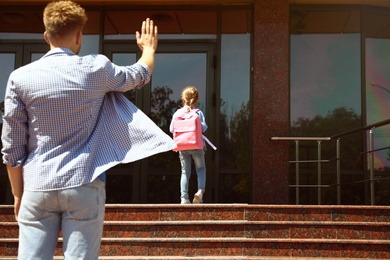 Photo of Young father seeing his little child off to school outdoors