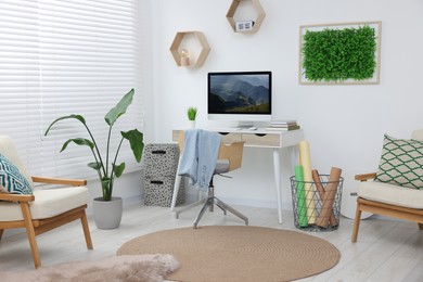 Photo of Green artificial plant wall panel and desk with computer in light room. Interior design