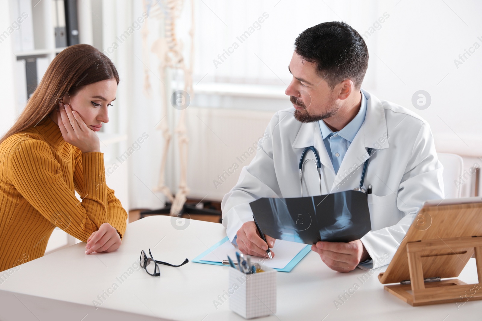 Photo of Orthopedist showing X-ray picture to patient at table in clinic