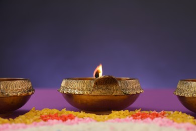 Photo of Diwali celebration. Diya lamps and colorful rangoli against purple background, closeup