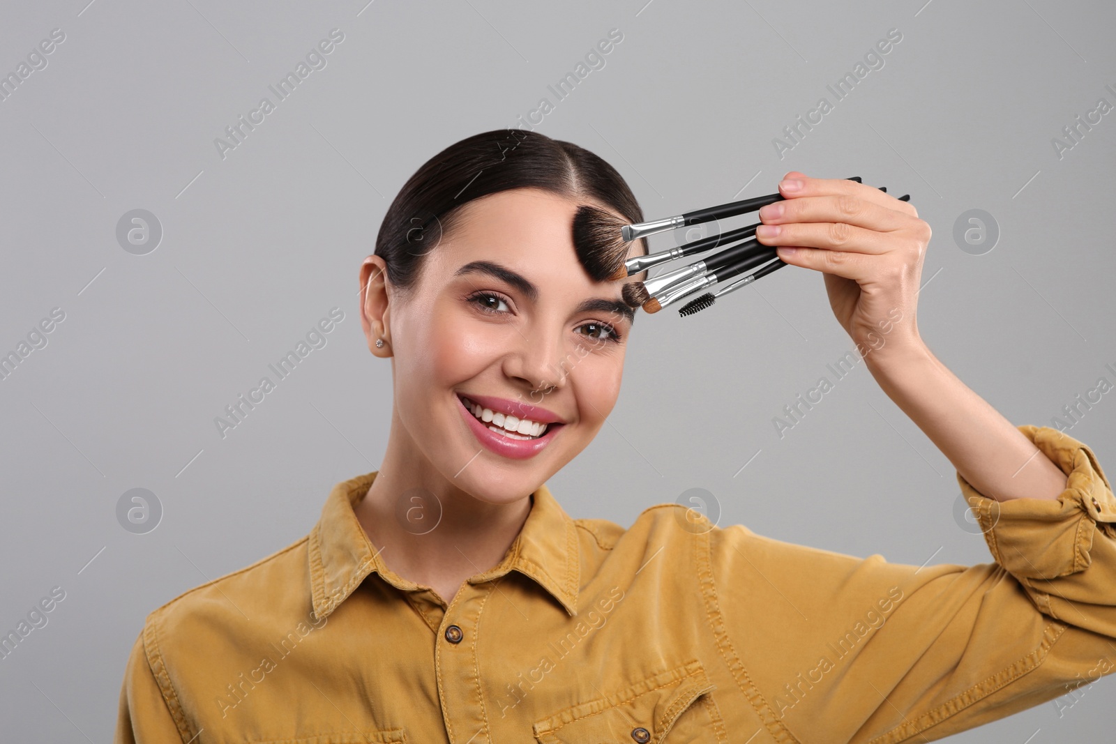 Photo of Happy woman with different makeup brushes on light grey background