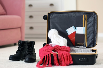 Modern suitcase with warm clothes on floor indoors