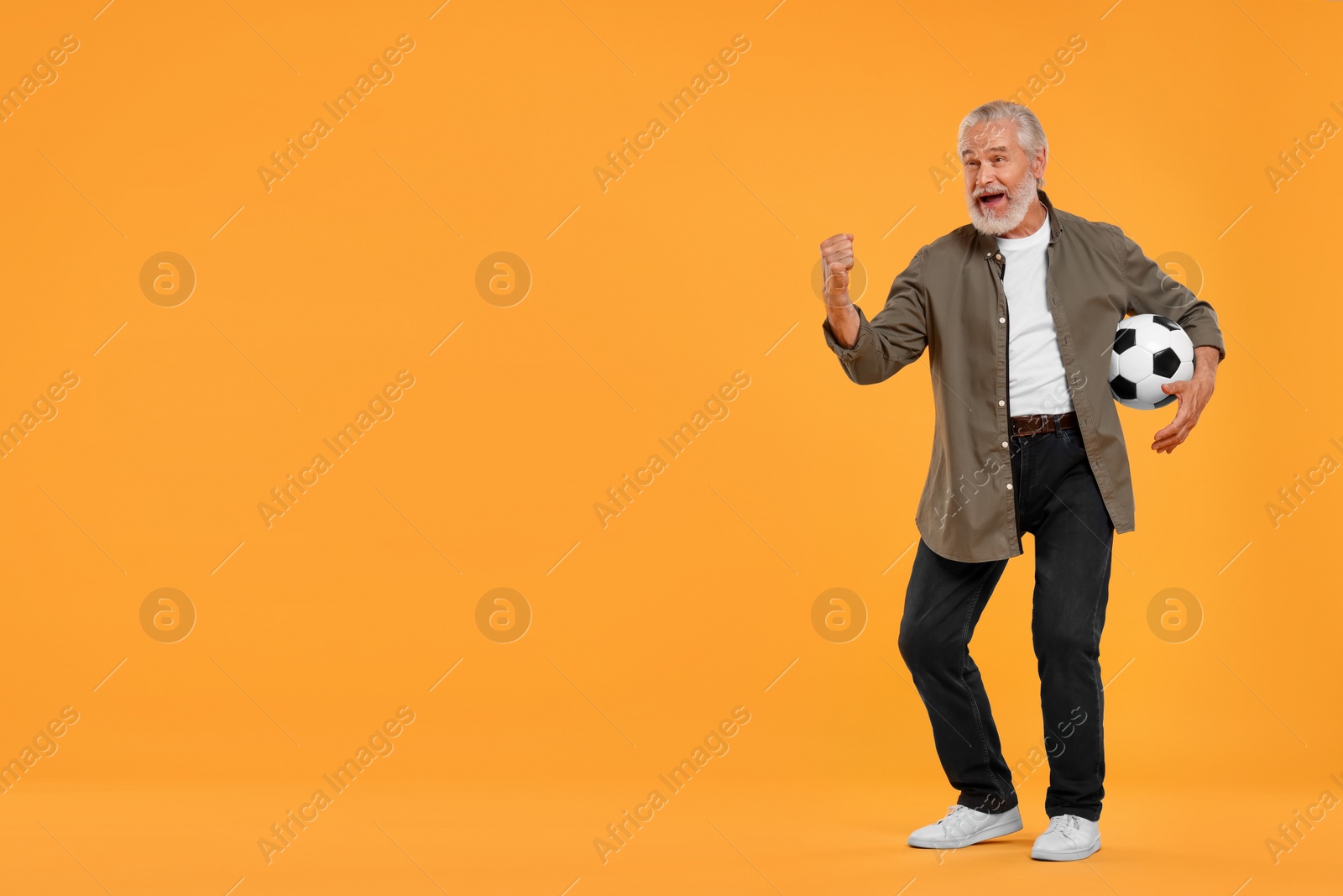 Photo of Emotional senior sports fan with soccer ball on yellow background, space for text