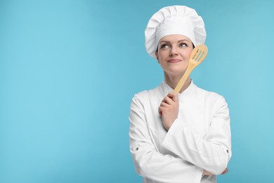 Photo of Happy chef in uniform holding wooden spatula on light blue background, space for text