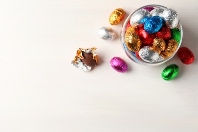 Glass jar with chocolate eggs wrapped in colorful foil on white table, flat lay. Space for text