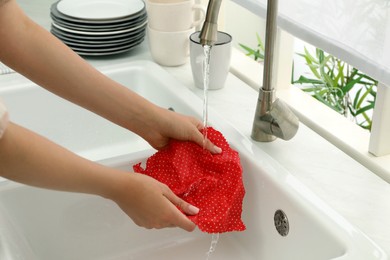 Photo of Woman washing beeswax food wrap under tap water in kitchen sink, closeup