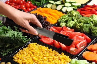 Young woman taking tomatoes from salad bar, closeup