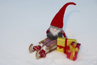 Photo of Wooden sleigh with Christmas gnome and gift boxes on snow outdoors