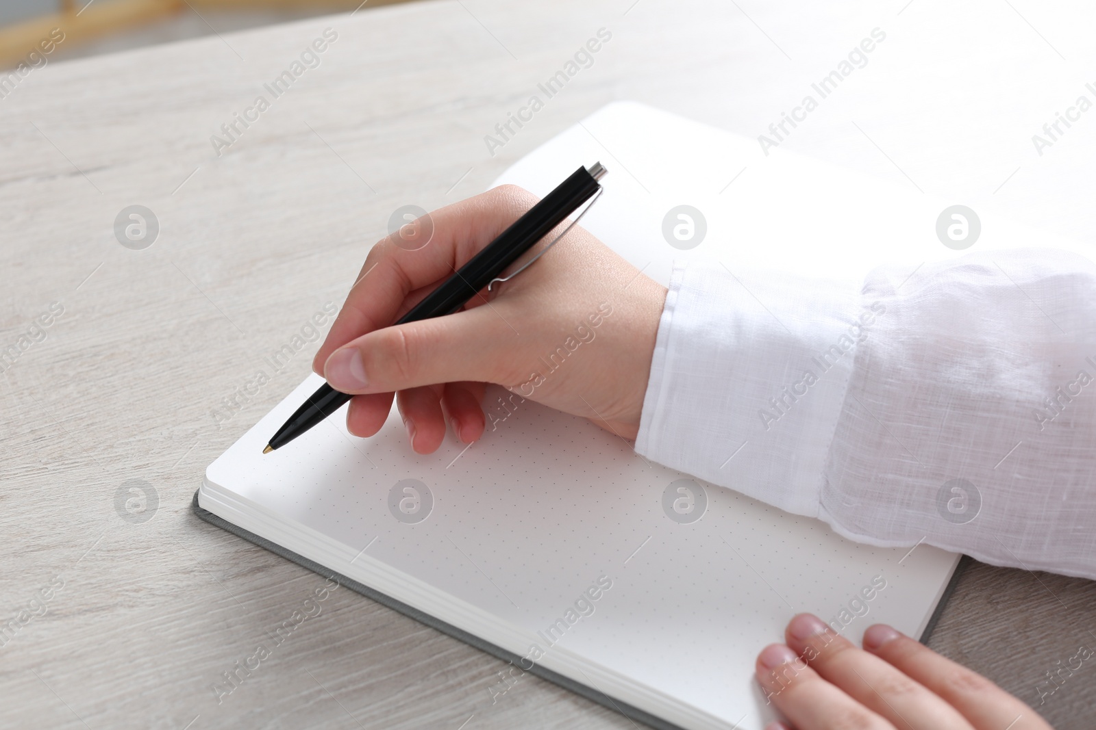 Photo of Woman writing in notebook at wooden table in office, closeup