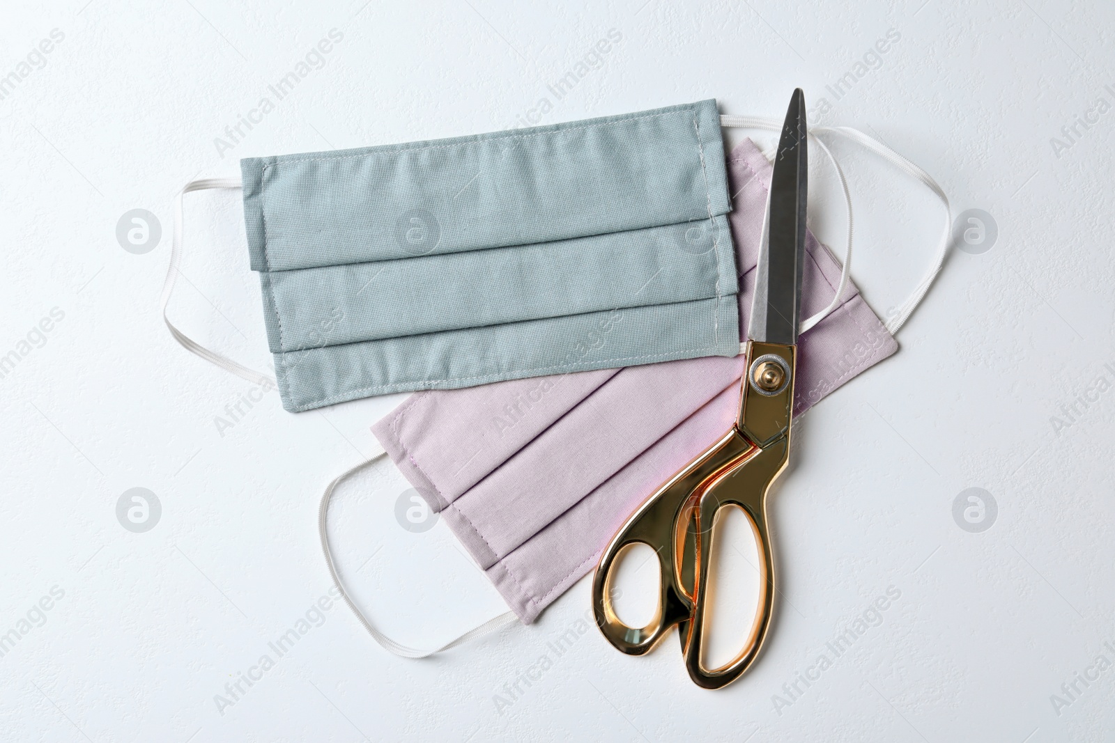 Photo of Homemade protective masks and scissors on white background, flat lay. Sewing idea