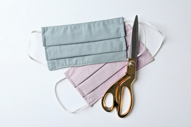 Homemade protective masks and scissors on white background, flat lay. Sewing idea