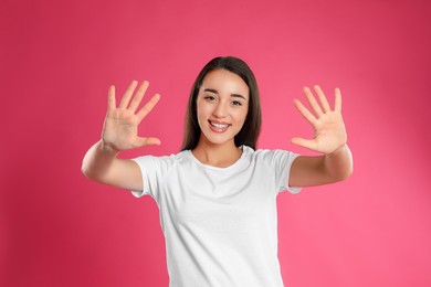 Photo of Woman showing number ten with her hands on pink background