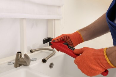 Photo of Man with pipe wrench near sink in kitchen, closeup. Water tap installation