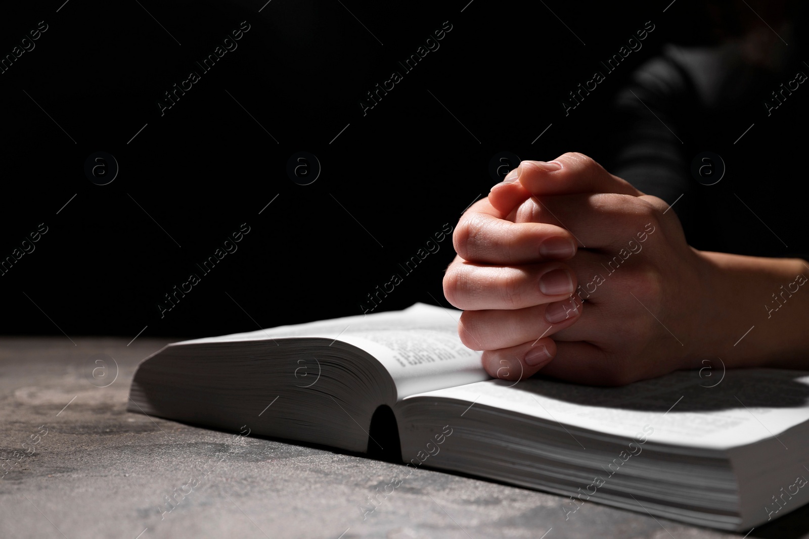 Photo of Religion. Christian woman praying over Bible at table against black background, closeup. Space for text