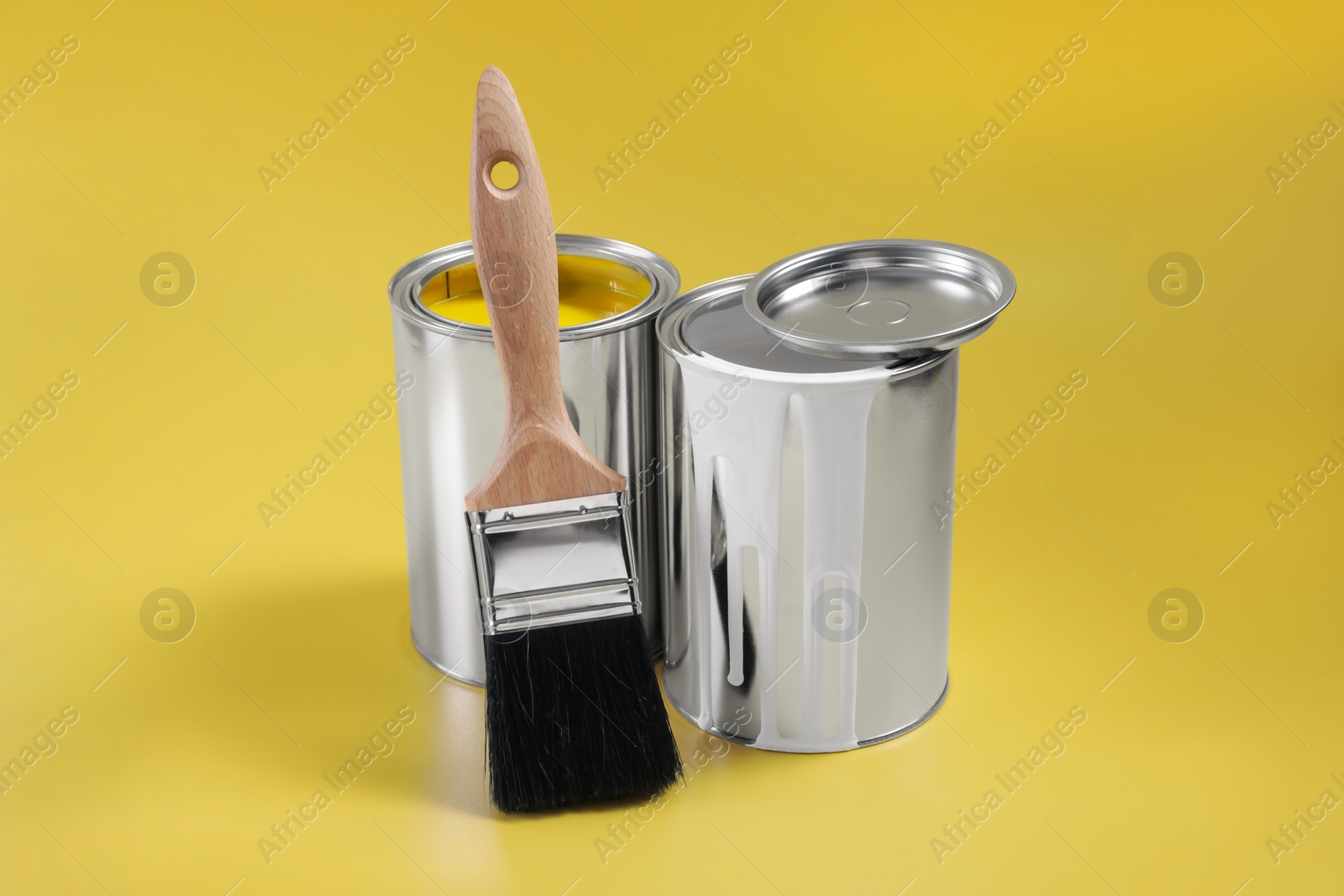 Photo of Cans of paints and brush on yellow background