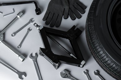Photo of Car wheel, scissor jack, gloves and different tools on grey background, flat lay