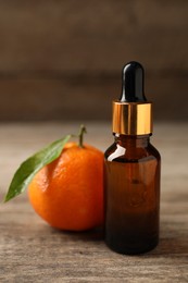 Photo of Bottle of tangerine essential oil and fresh fruit on wooden table