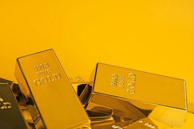 Photo of Many shiny gold bars on orange background, closeup. Space for text